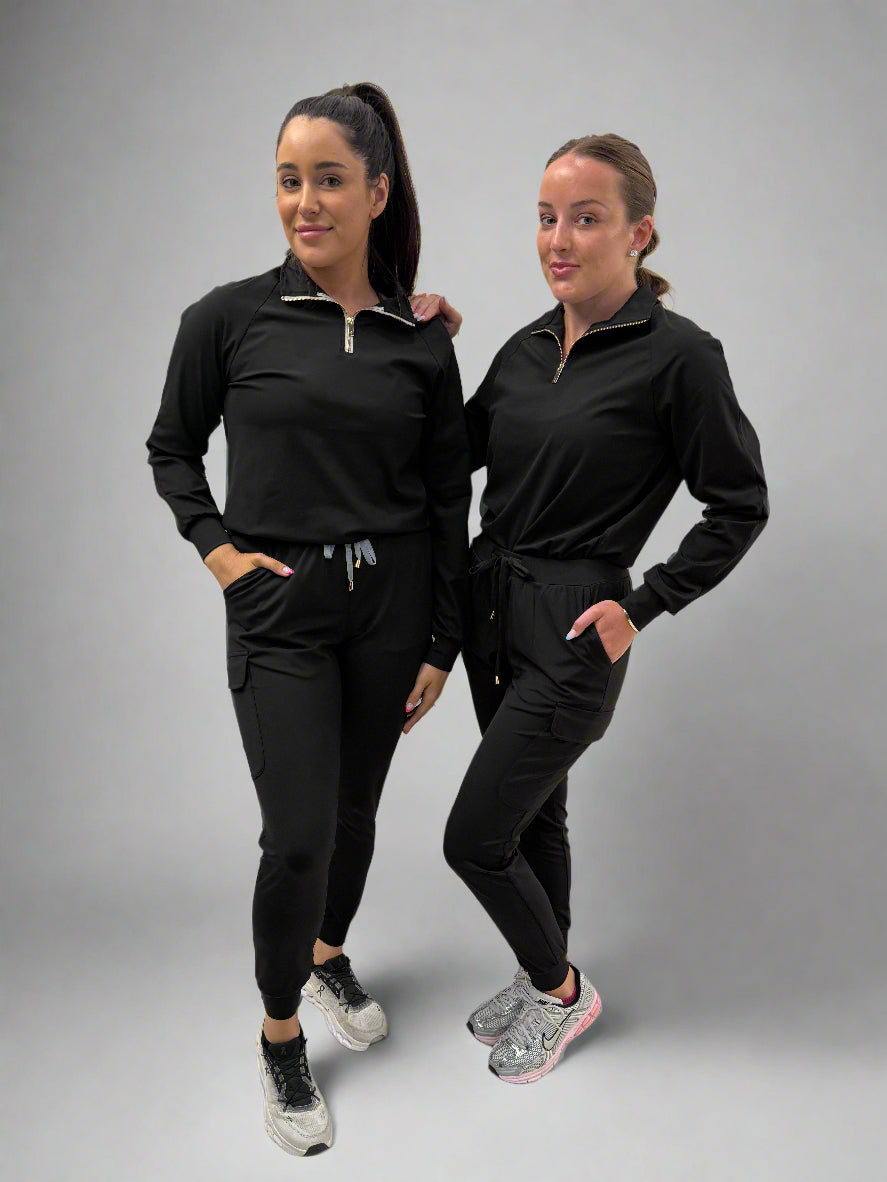 Two women wearing matching black athletic outfits on a gray background