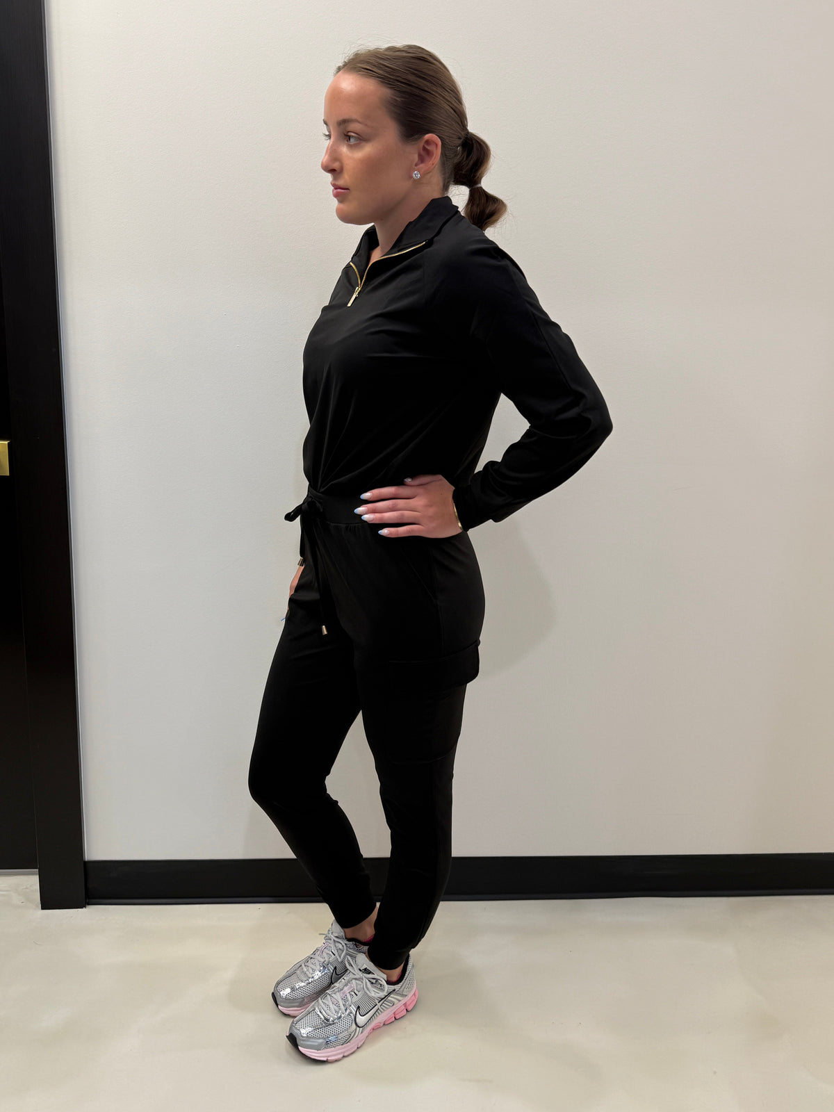Person wearing a black outfit with white sneakers on a plain background