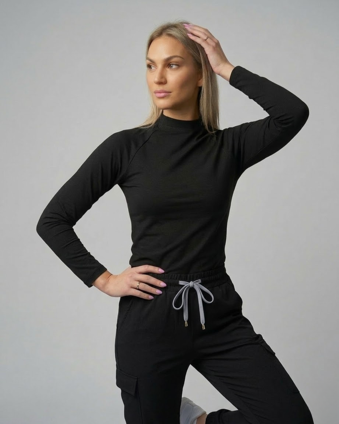 Woman wearing a black long-sleeve top and black pants with gray drawstrings on a gray background