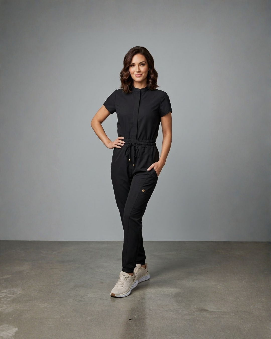 Woman wearing a black jumpsuit standing against a gray background