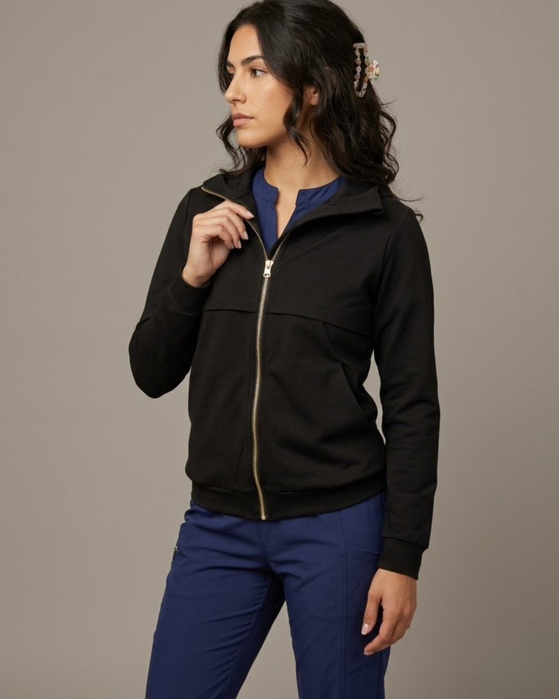 Woman wearing a black jacket and blue pants against a gray background