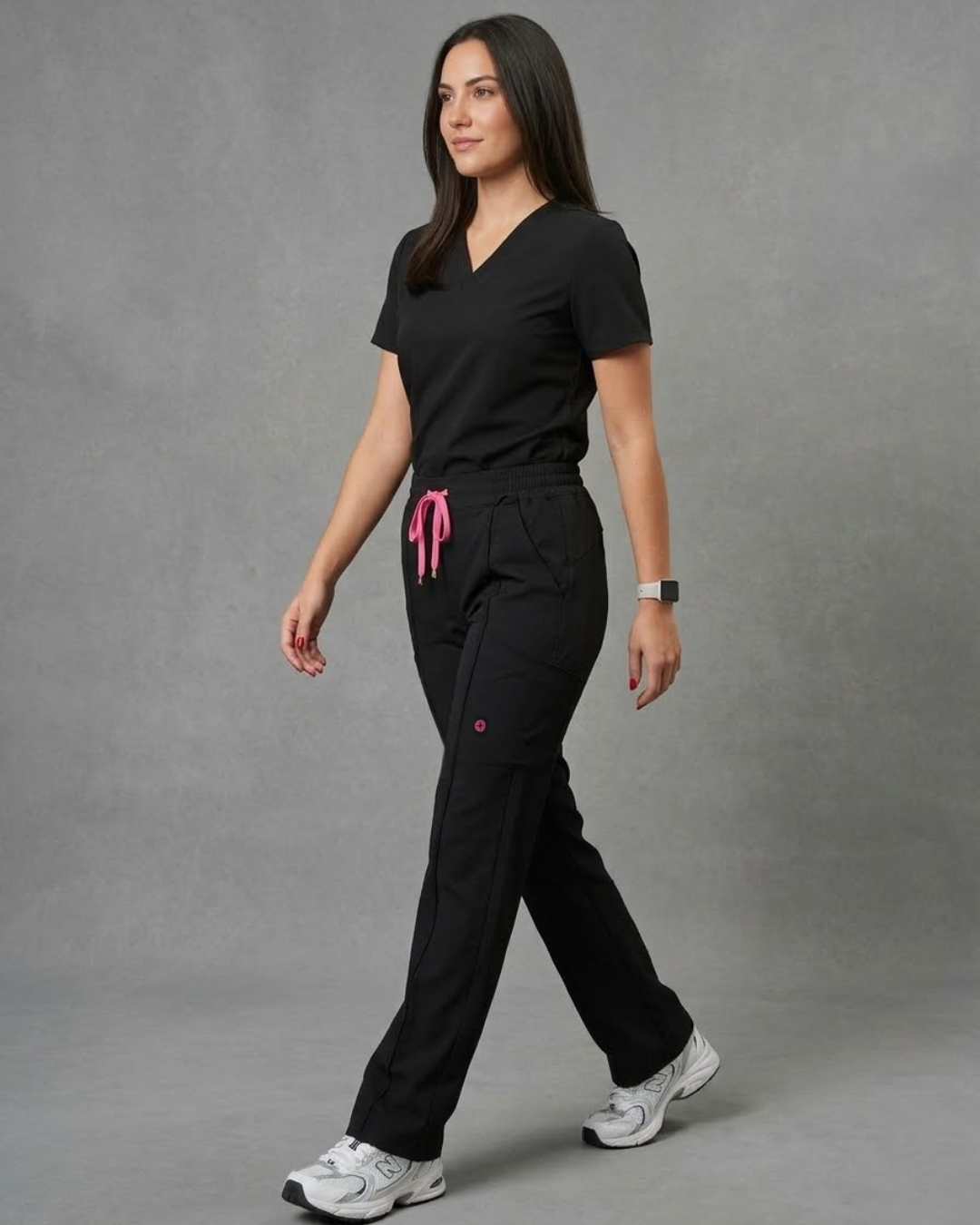 Woman wearing a black scrub set with pink accents on a gray background