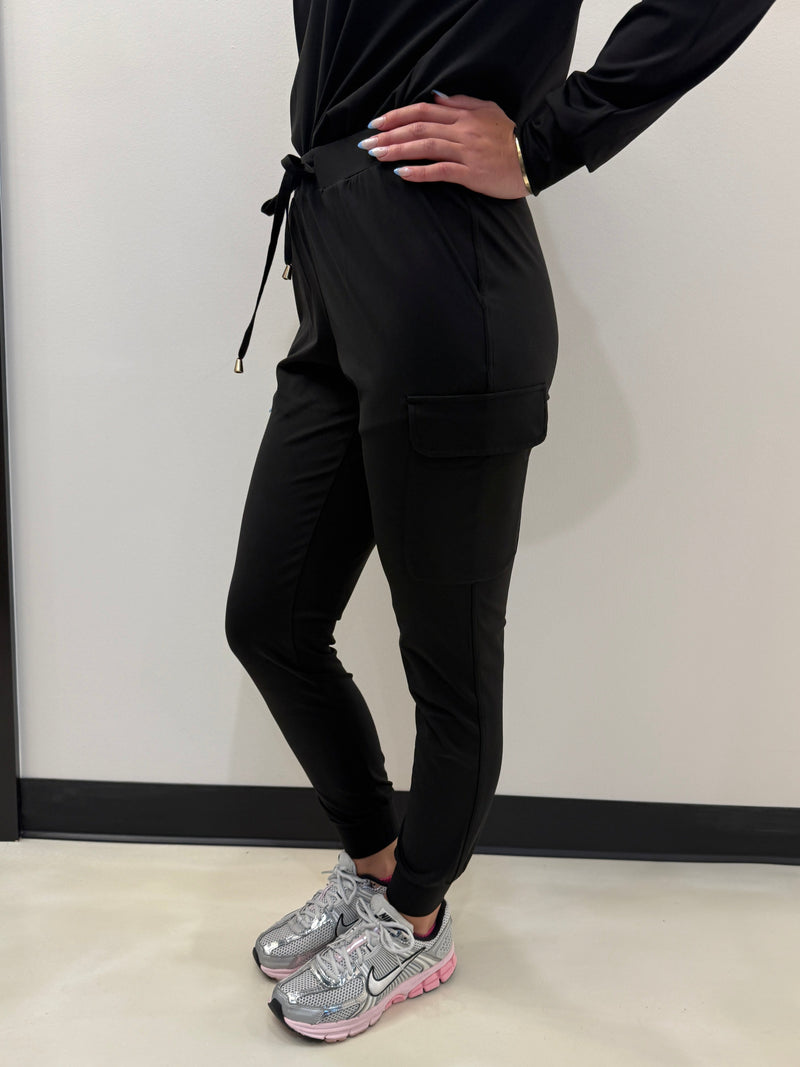 Person in black athletic wear with pink sneakers stretching on a white wall.