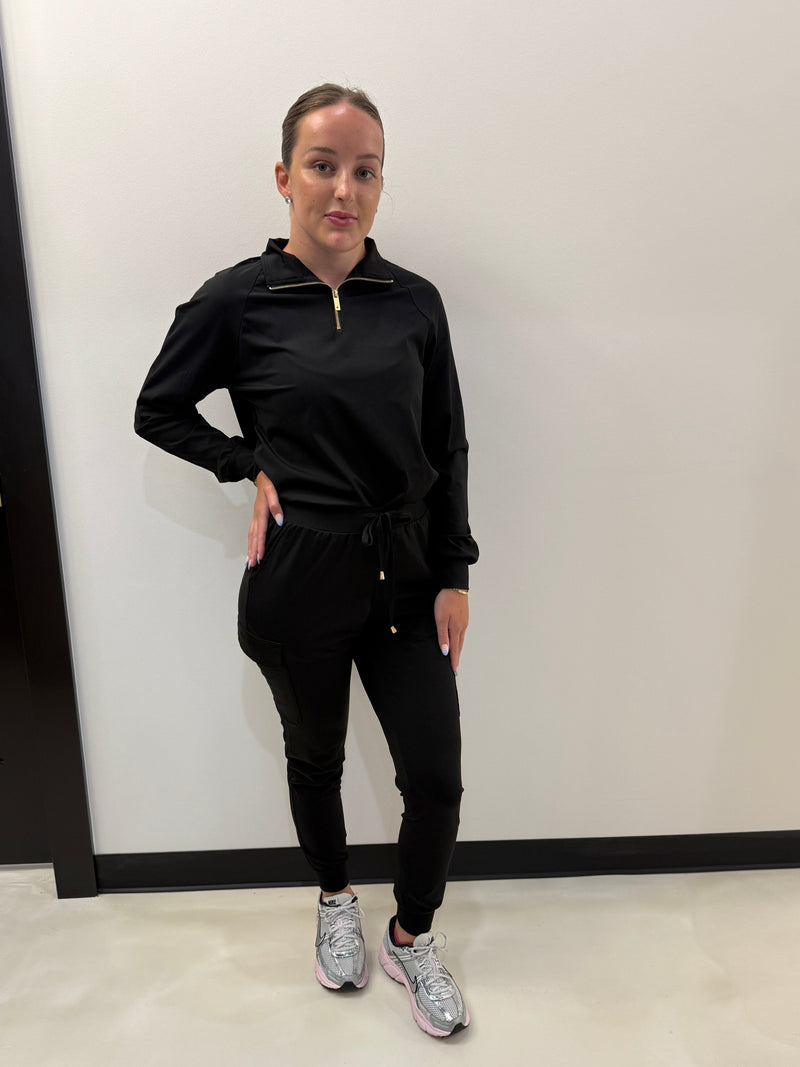 Person wearing a black outfit standing in front of a mirror on a white floor.