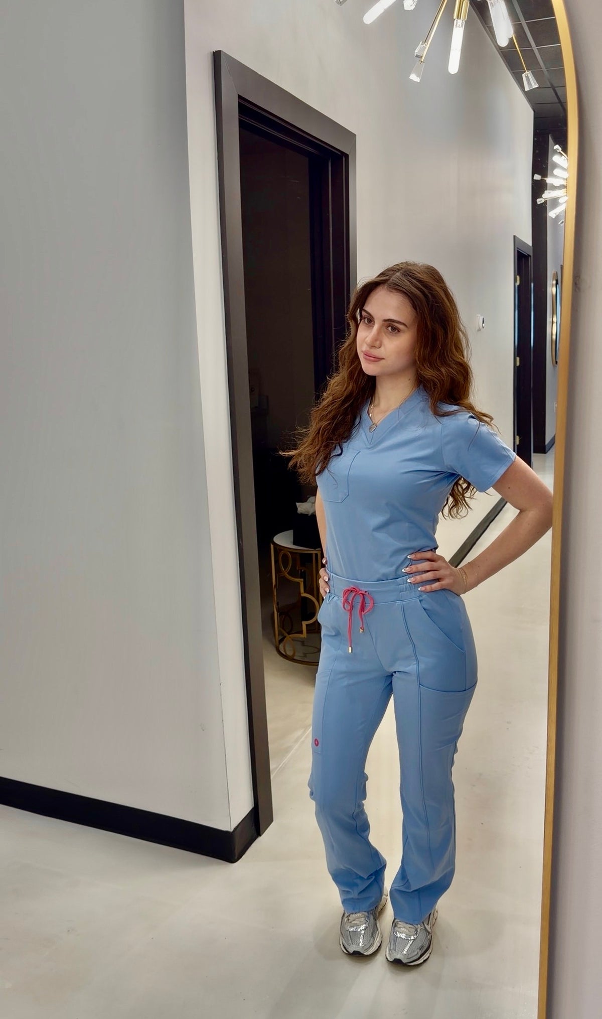 Woman in a blue medical scrubs set standing in front of a mirror.